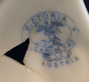 European hard paste porcelain ring holder decorated with a floral decal and gold gilt. Printed mark “Victoria Carlsbad Austria” dates 1891-1918. Similar example shown right.